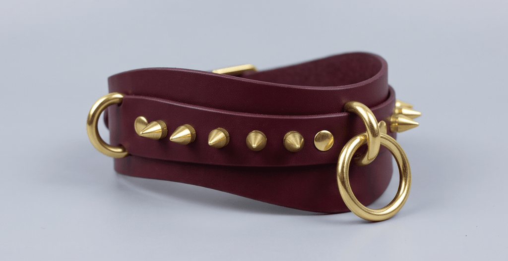 A burgundy leather choker necklace with gold studs and a gold ring.