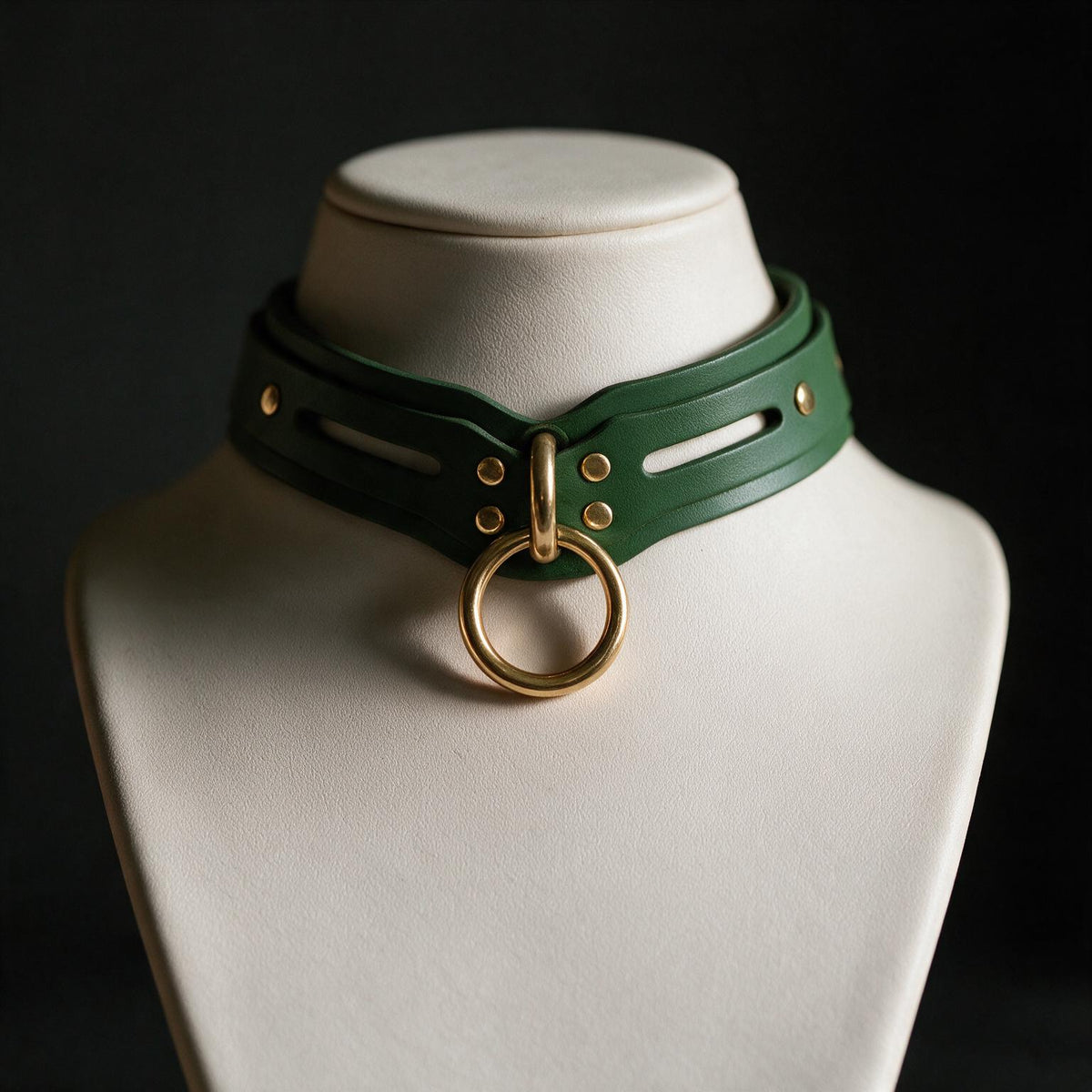 A close-up view of a green leather choker necklace with a gold ring and buckle, displayed on a white bust form against a dark background.