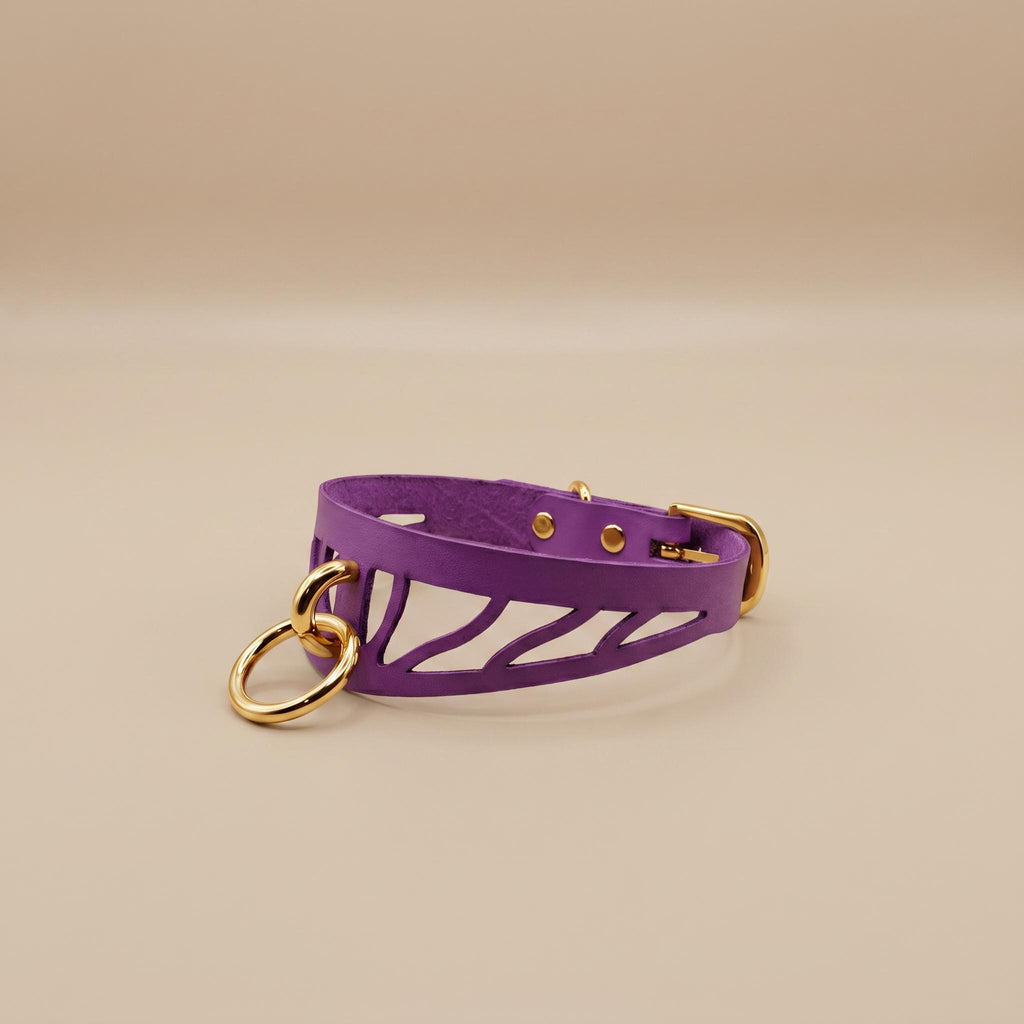 A purple leather choker collar with a cutout design and two gold-colored rings on the front.