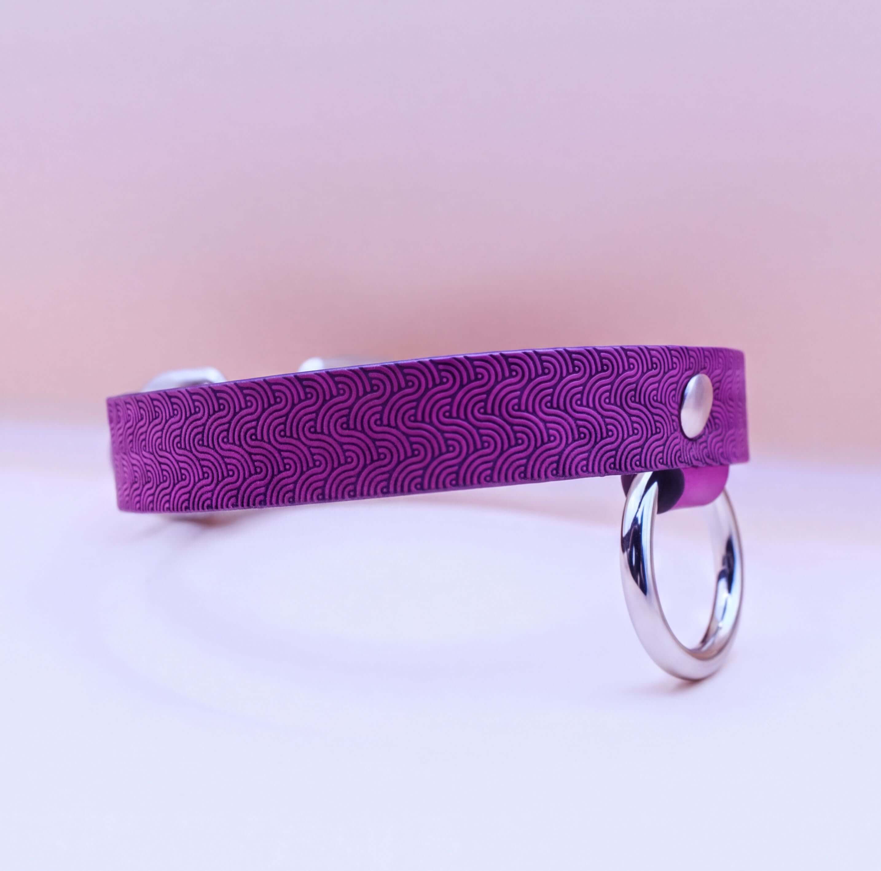 A purple patterned collar with a silver ring attached, resting on a white surface.