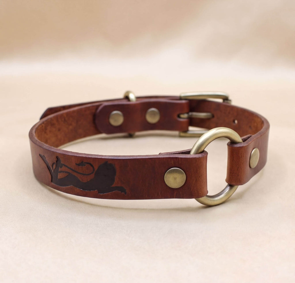 A brown leather dog collar with a metal buckle and a lion design on the side.