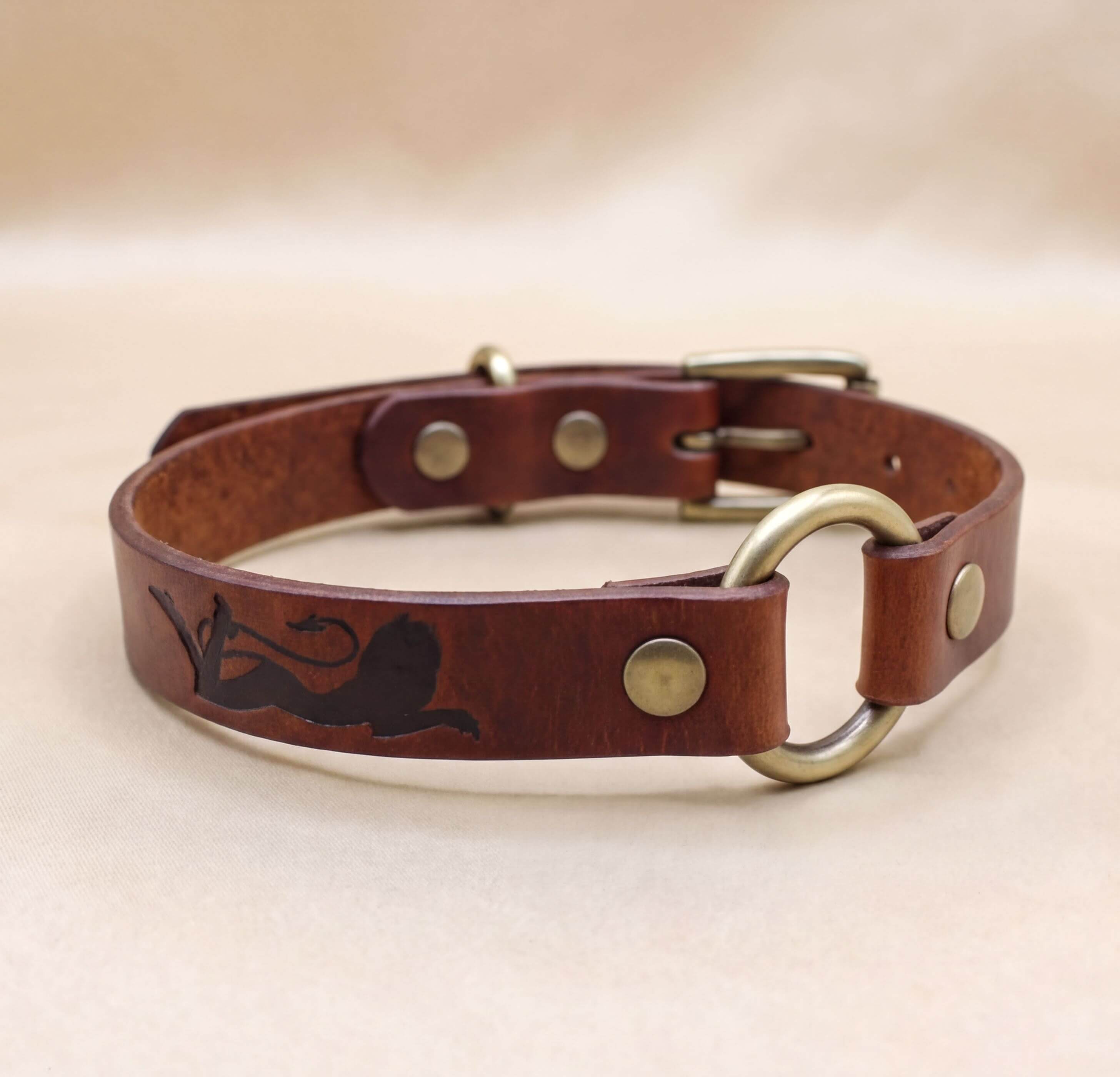 A brown leather dog collar with a metal buckle and a lion design on the side.