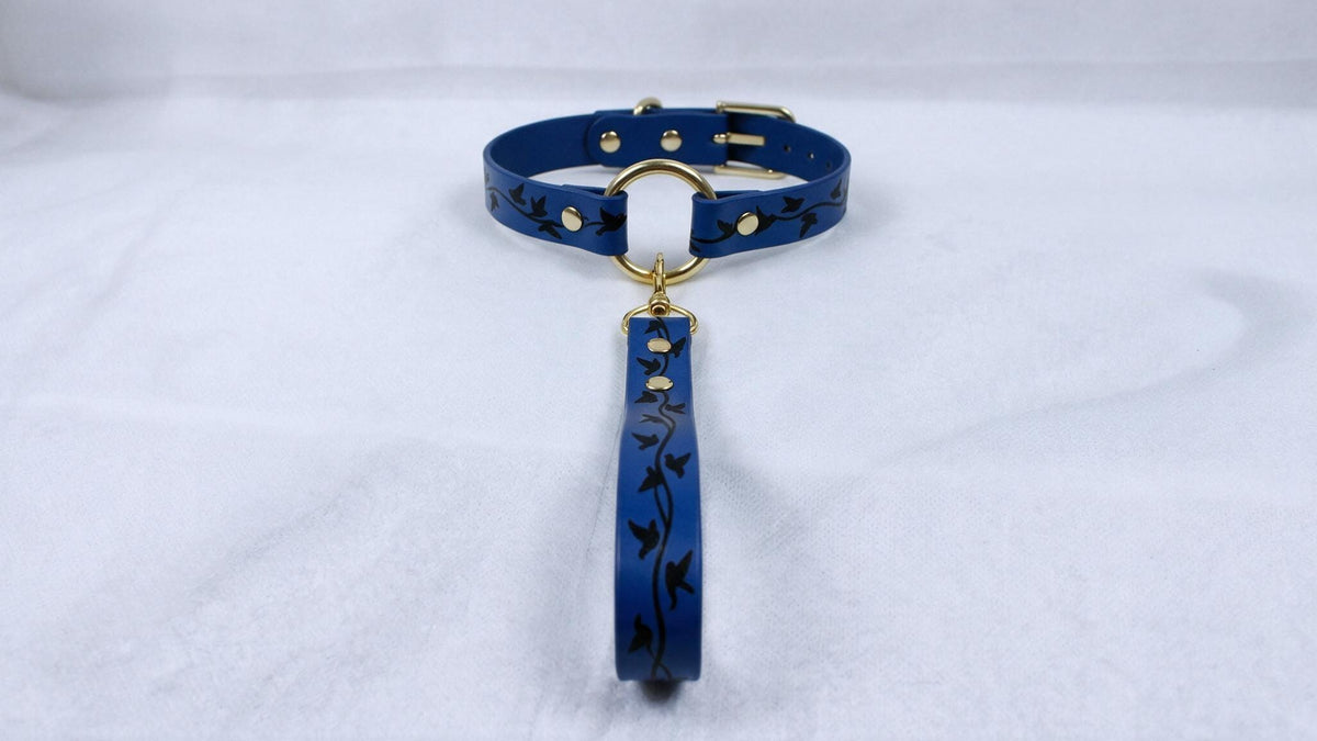 A blue collar with a gold-colored buckle and a black floral pattern on the strap is displayed against a white background.