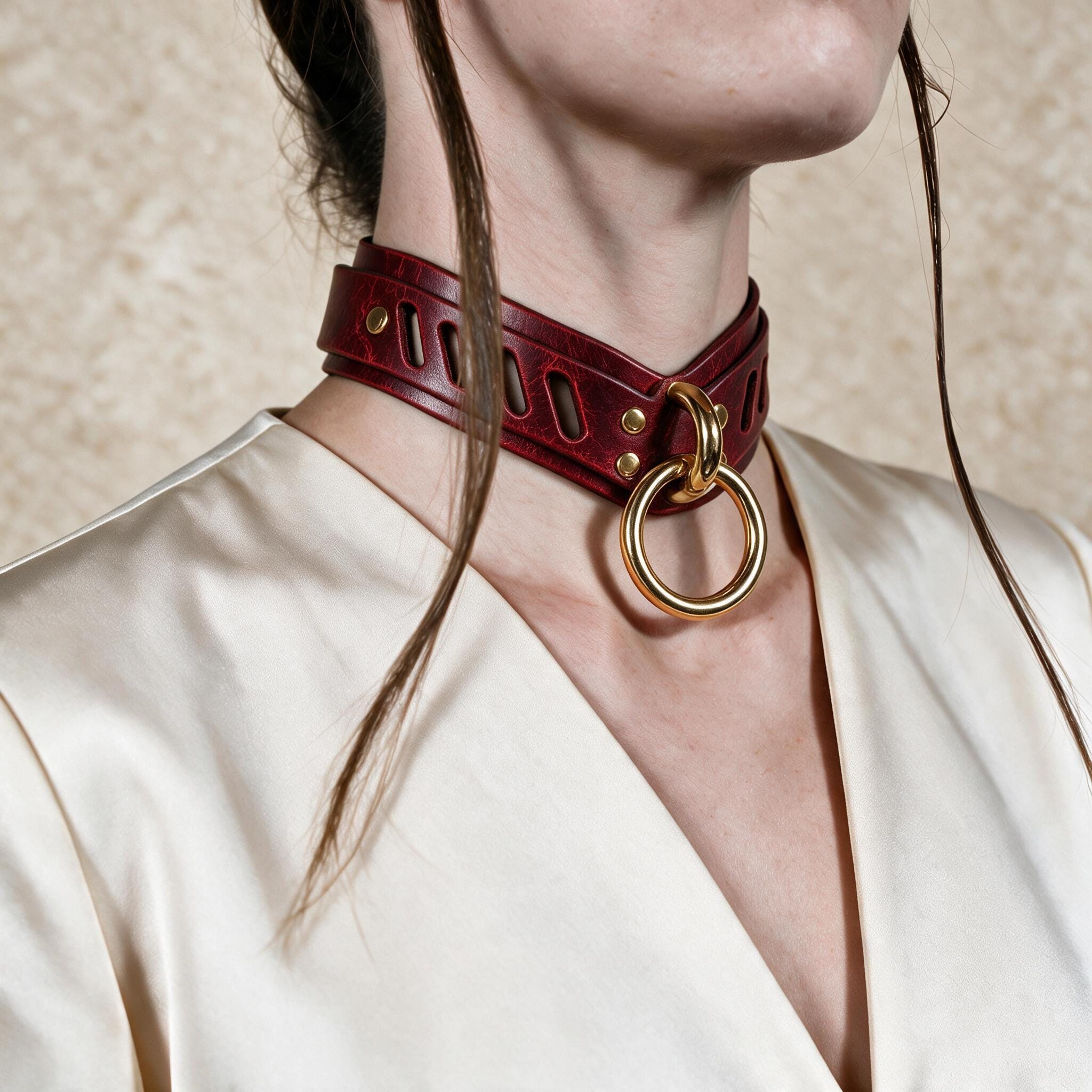 A close-up of a person wearing a burgundy leather choker necklace with a gold ring, against a plain background.