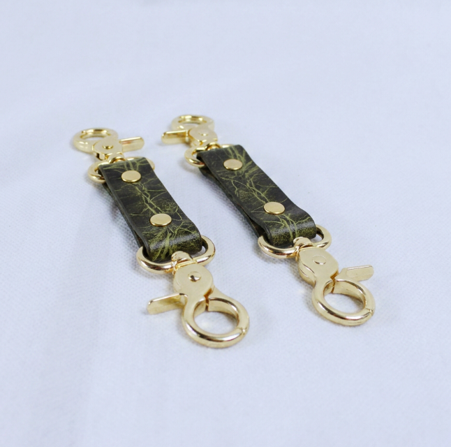 a pair of gold-colored leather straps with metal clasps and hooks, placed on a white surface.