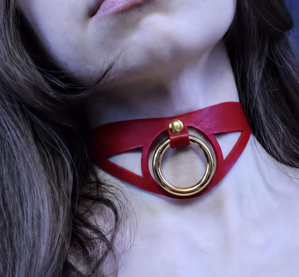 A close-up of a woman's neck with a red choker necklace featuring a gold ring.