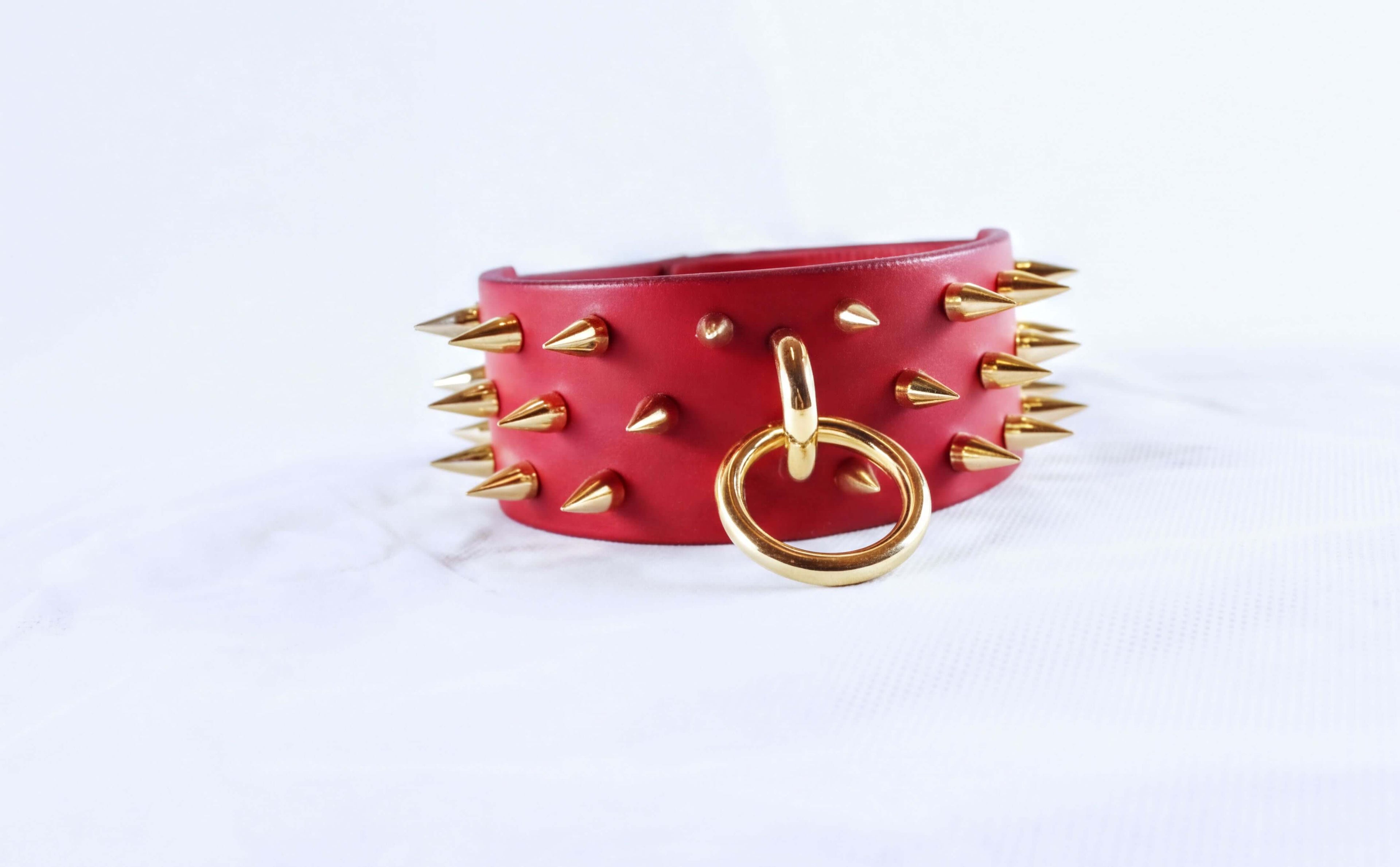A red leather choker necklace with gold spikes and a gold ring is displayed against a white background.