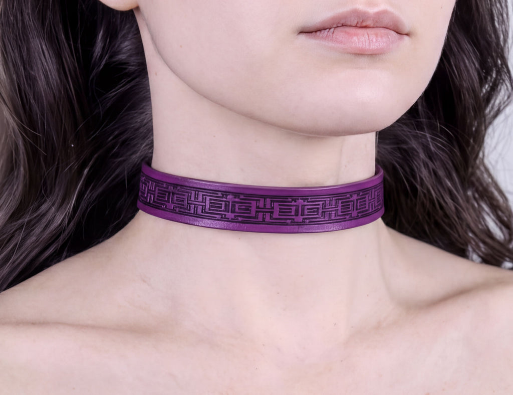 A close-up of a person's neck and chest area wearing a purple choker necklace with a geometric pattern.