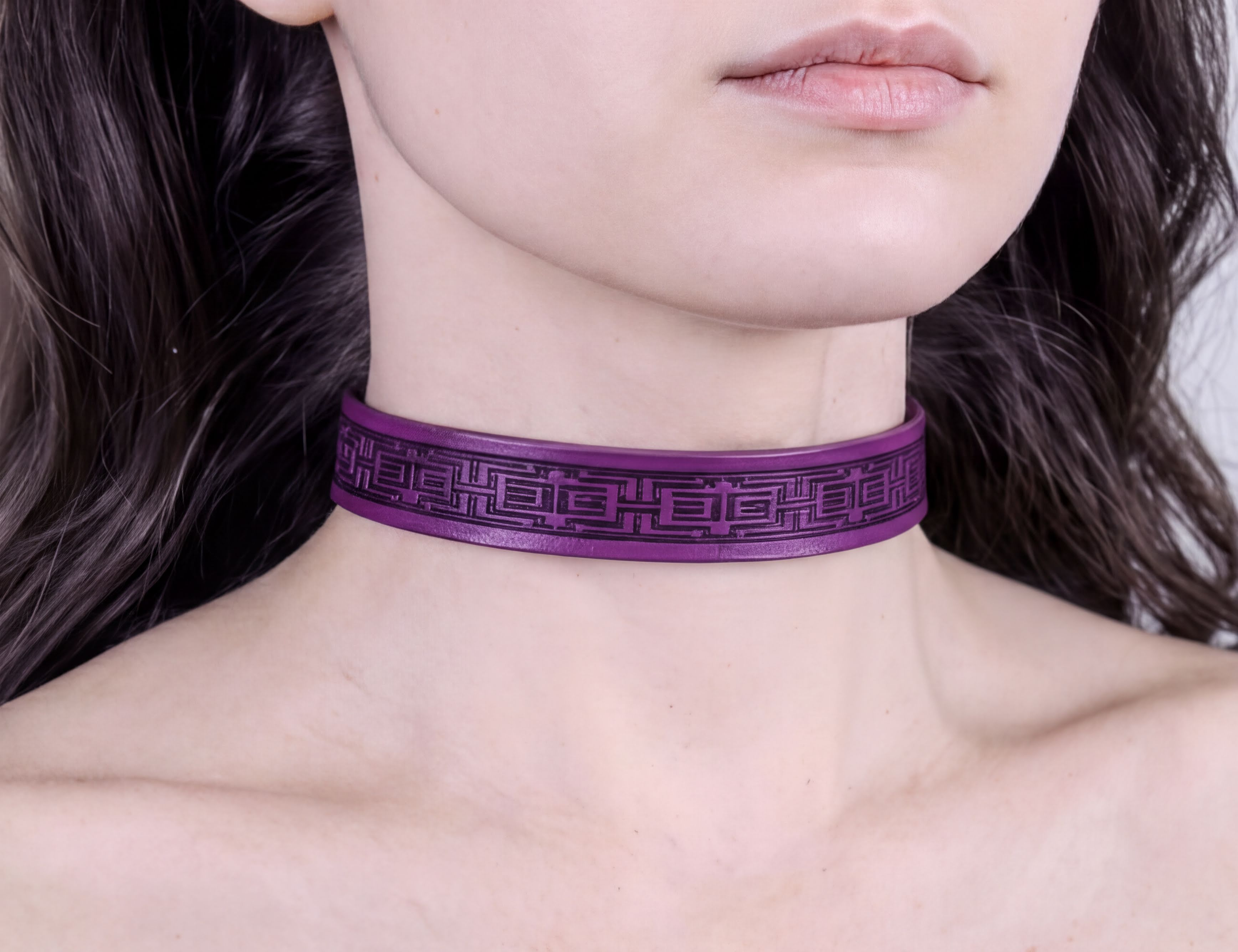 A close-up of a person's neck and chest area wearing a purple choker necklace with a geometric pattern.