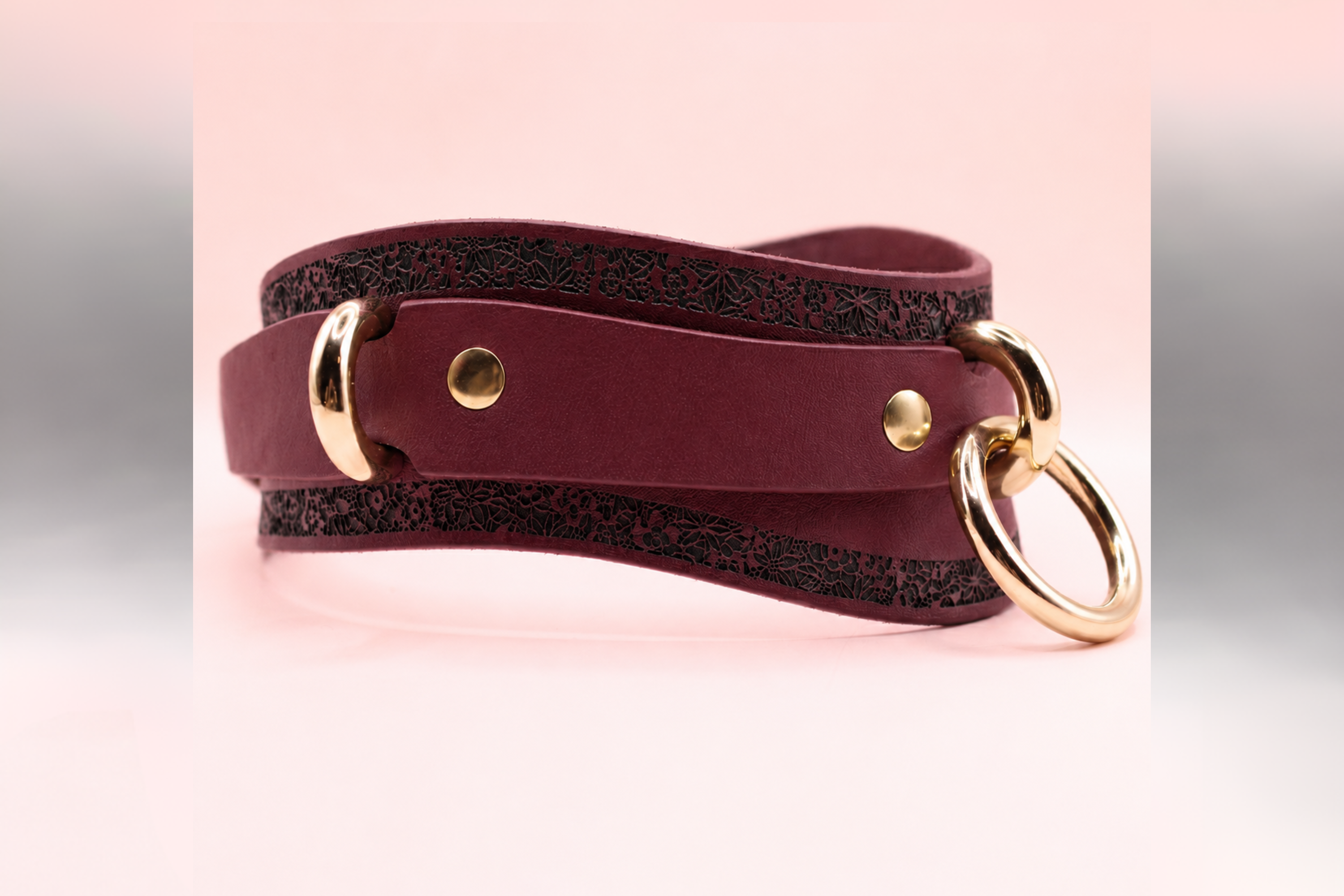 A burgundy leather choker necklace with a gold-colored buckle and two circular rings.