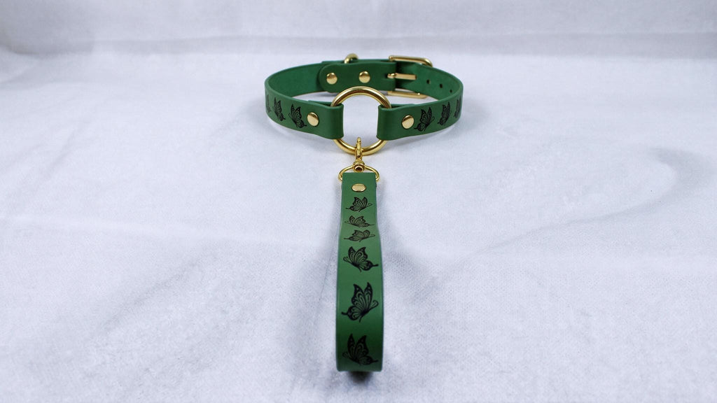 A green leather collar with a gold buckle and a black butterfly design on the strap.