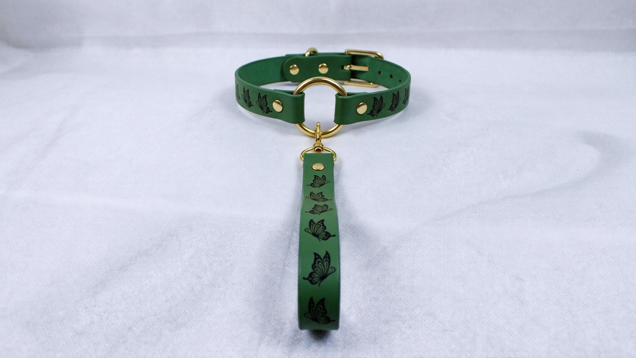 A green leather collar with a gold buckle and a black butterfly design on the strap.