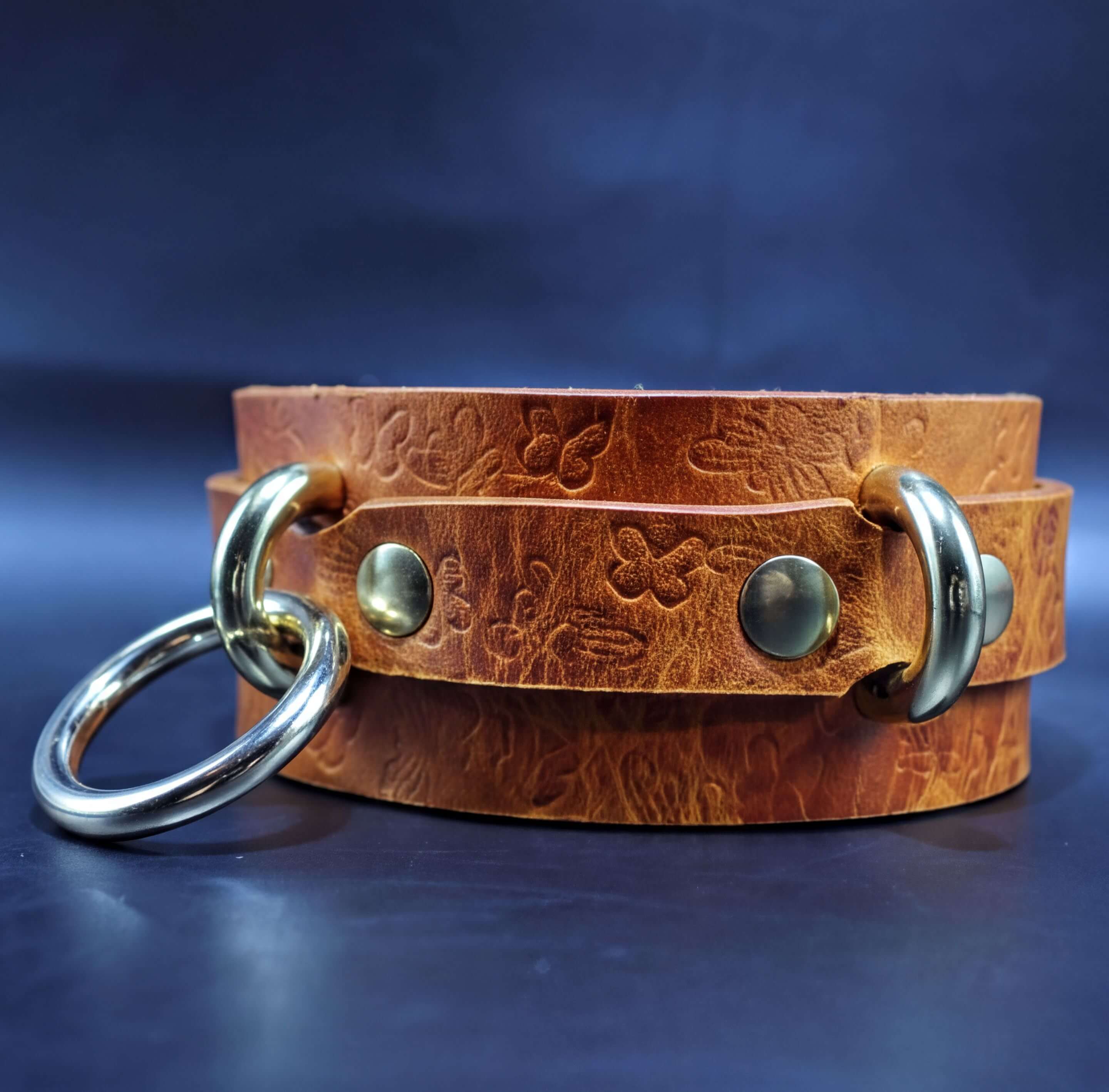 A brown leather choker necklace with metal rings and buckles, resting on a dark blue background.