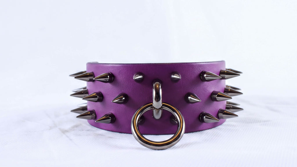 A purple leather choker necklace with spikes protruding from it and a metal ring in the center.