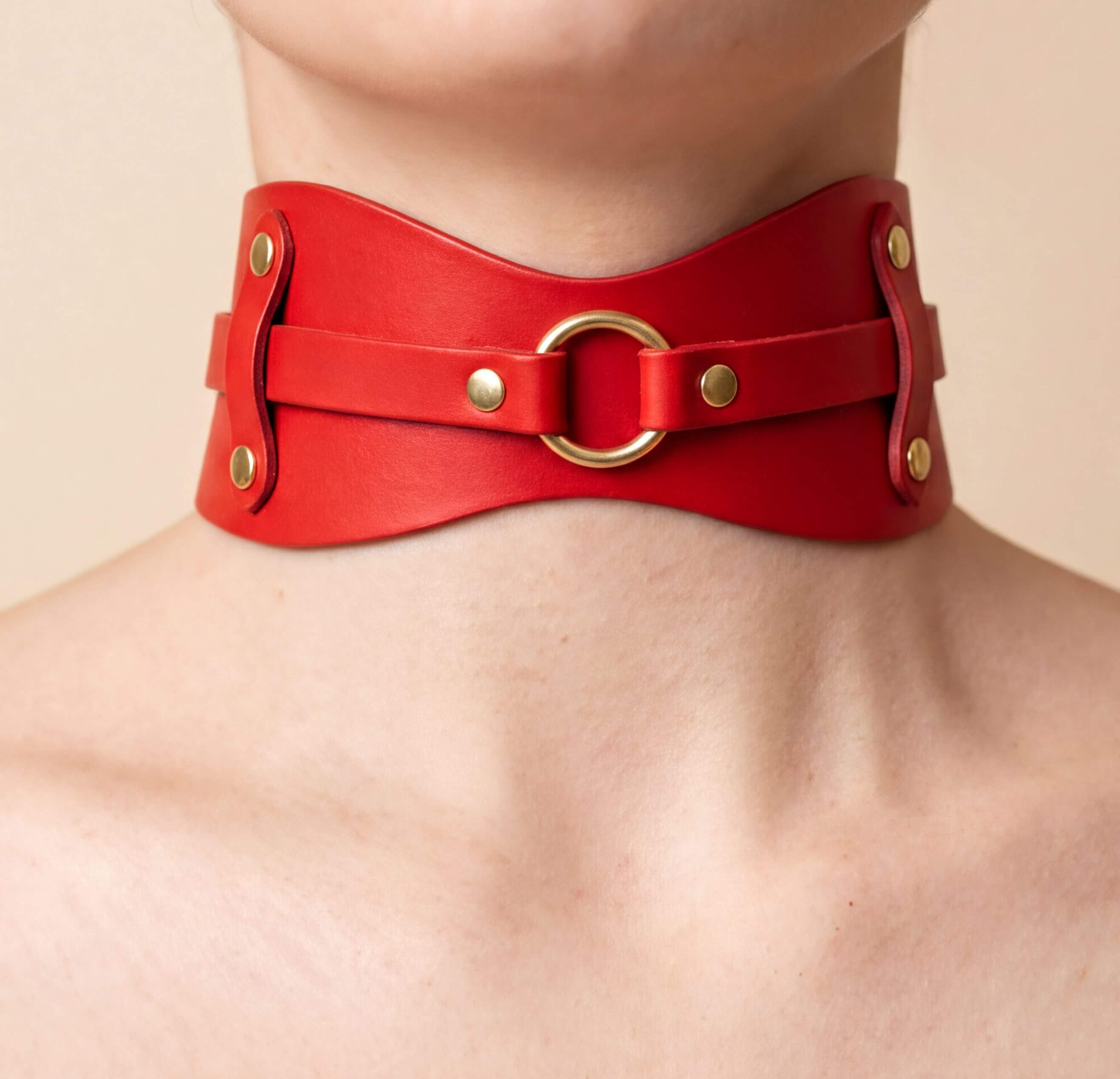 A close-up of a person's neck wearing a red leather choker necklace with a gold ring.
