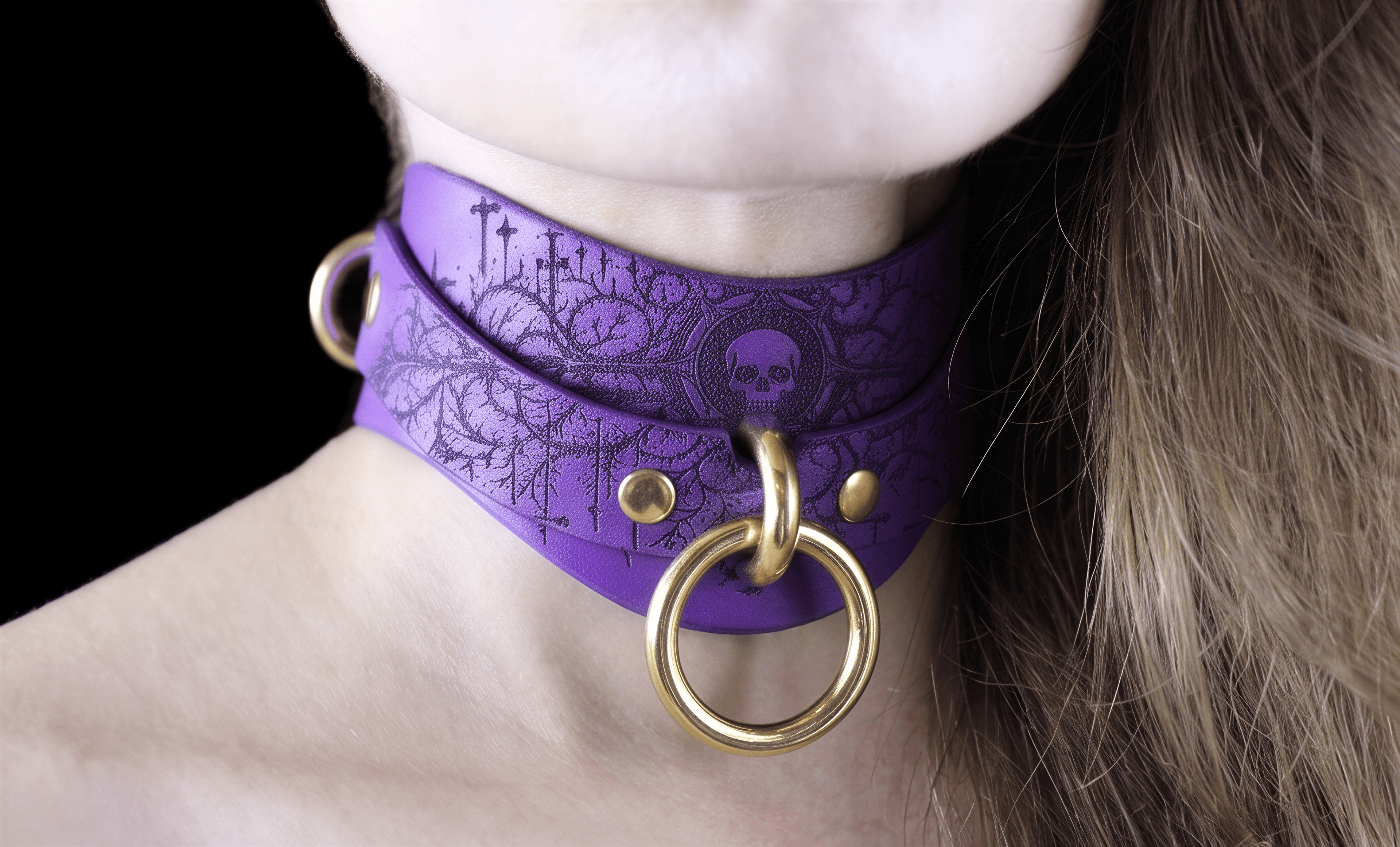 A close-up of a person's neck wearing a purple choker necklace with a skull design and gold-colored metal rings.