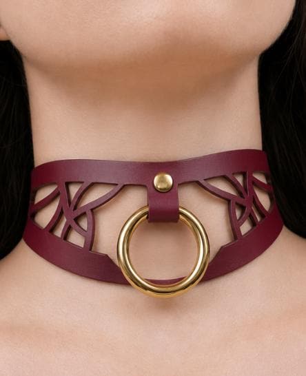 A close-up view of a woman's neck and chest area wearing a burgundy choker necklace with a gold ring.