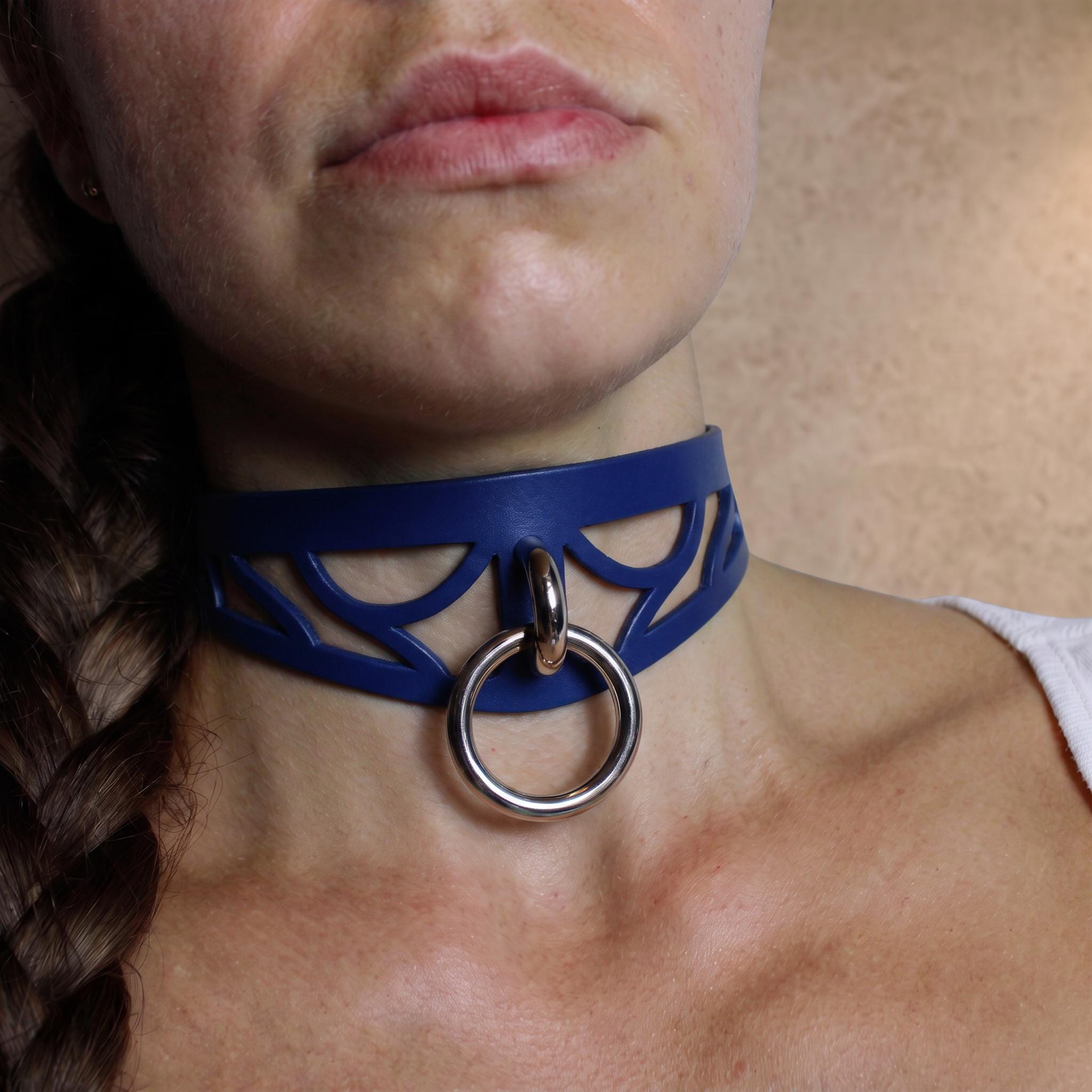 A close-up of a woman's neck and chest area, featuring a blue choker necklace with a metal ring and a braided hairstyle.