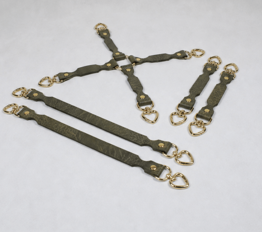 a collection of leather straps with gold-colored metal hardware, including heart-shaped buckles, arranged in various orientations.