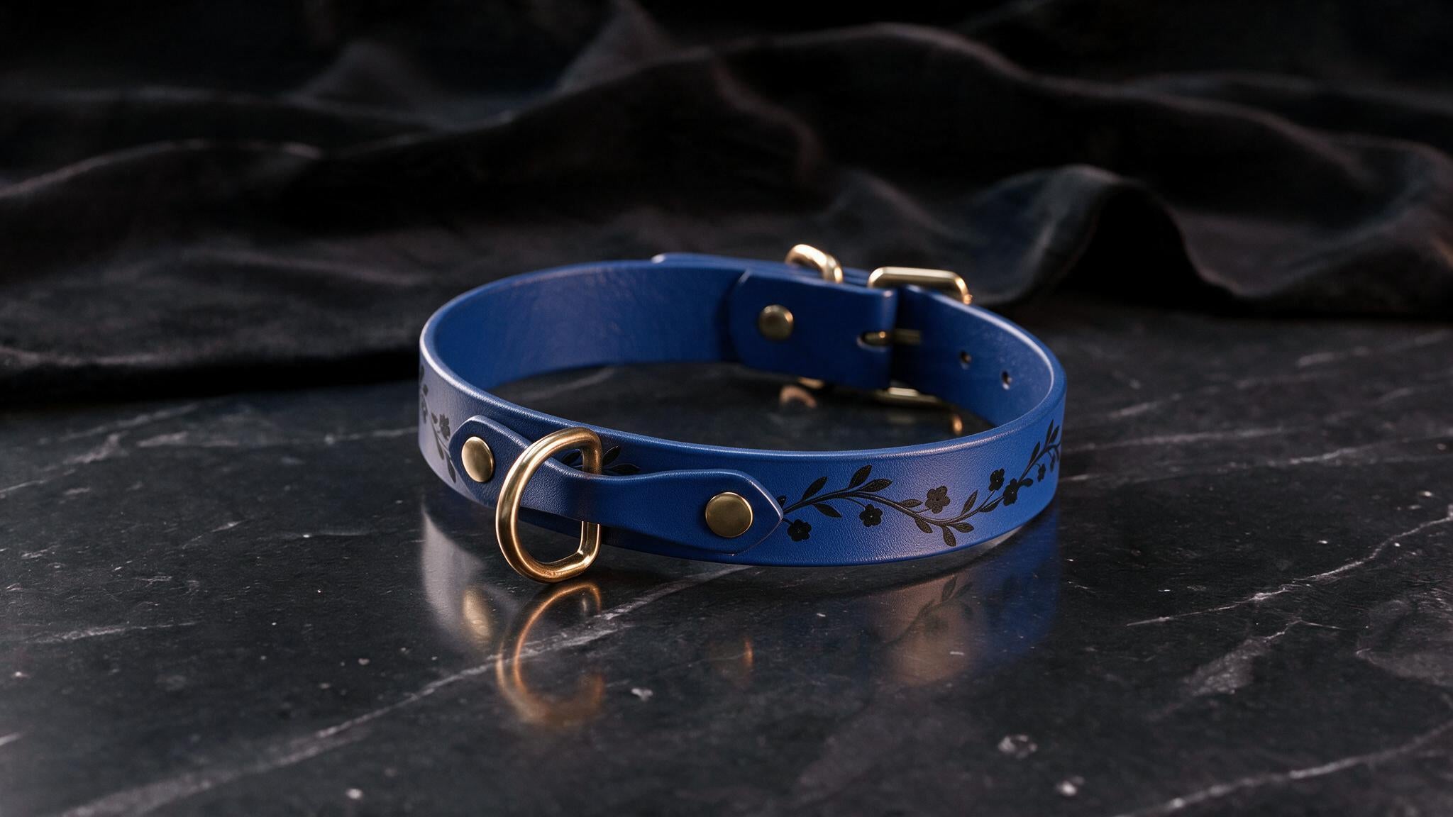 A blue leather collar with a floral design sits on a dark surface.