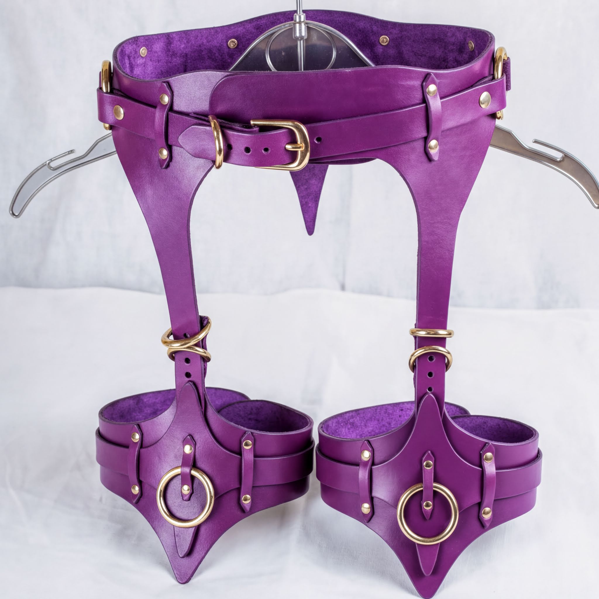 A pair of purple leather corsets with gold hardware, including buckles and straps, displayed on a white background.
