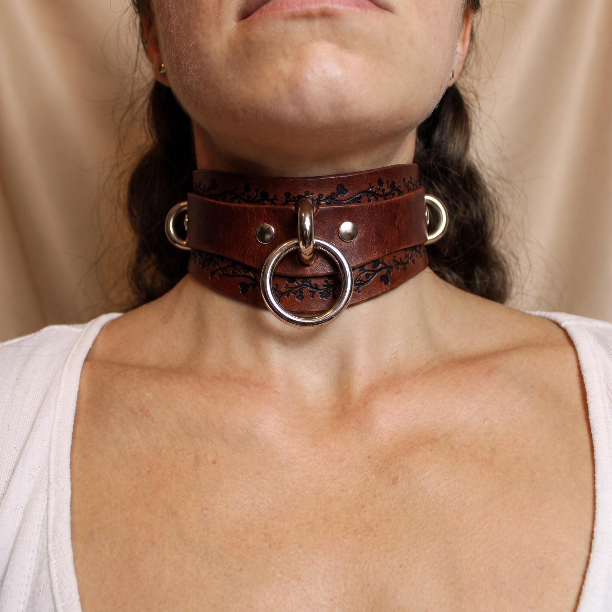 A close-up of a woman wearing a large, ornate leather choker necklace with a metal ring.