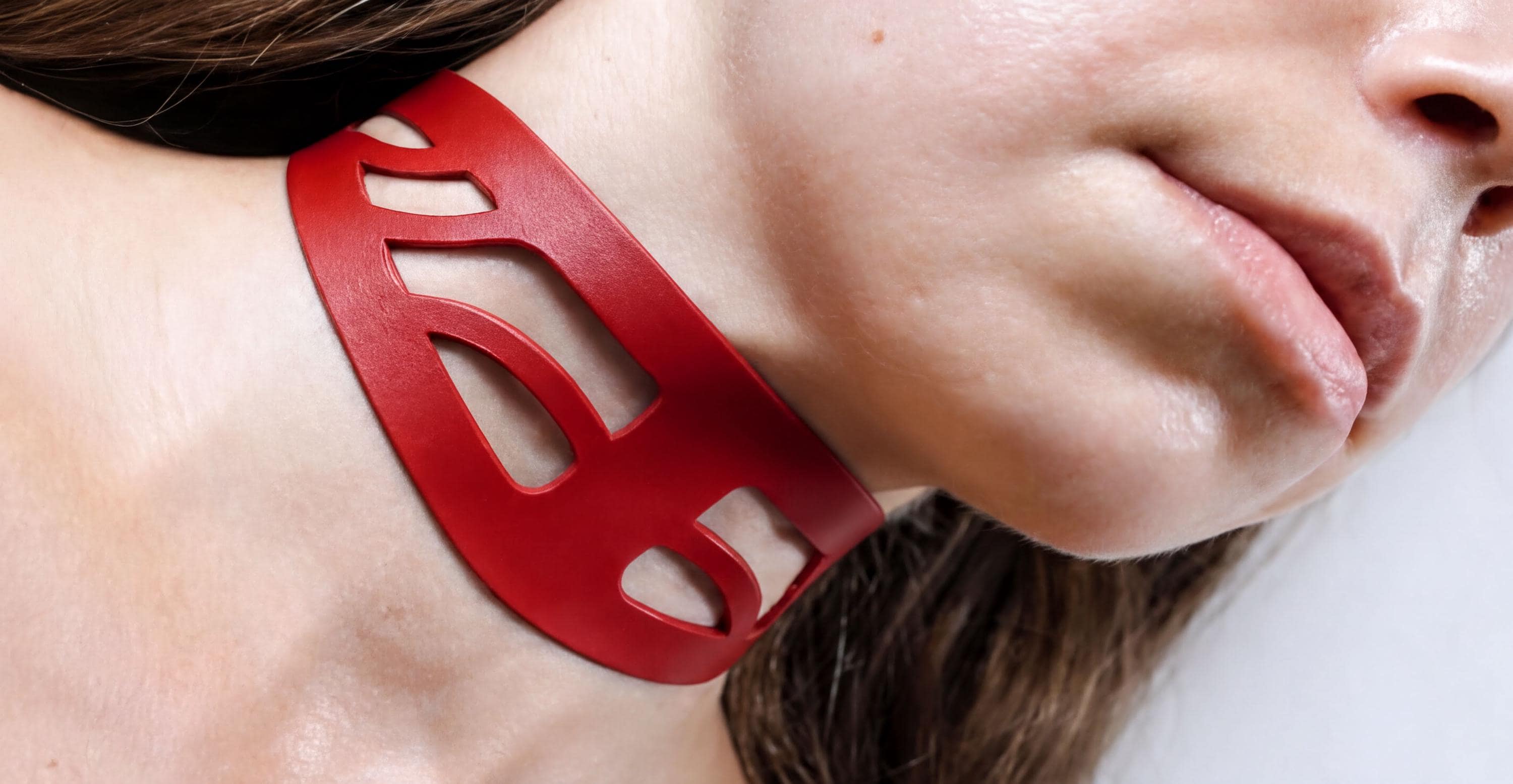 A close-up of a woman's neck and chin wearing a red, abstract-shaped necklace.