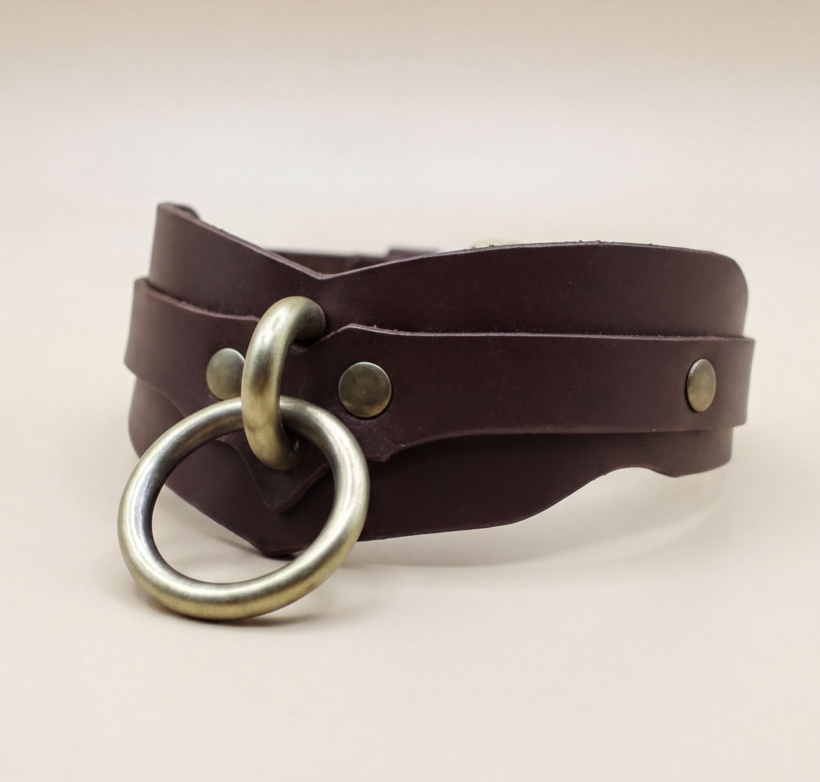 A brown leather choker necklace with a metal ring and two metal fasteners.