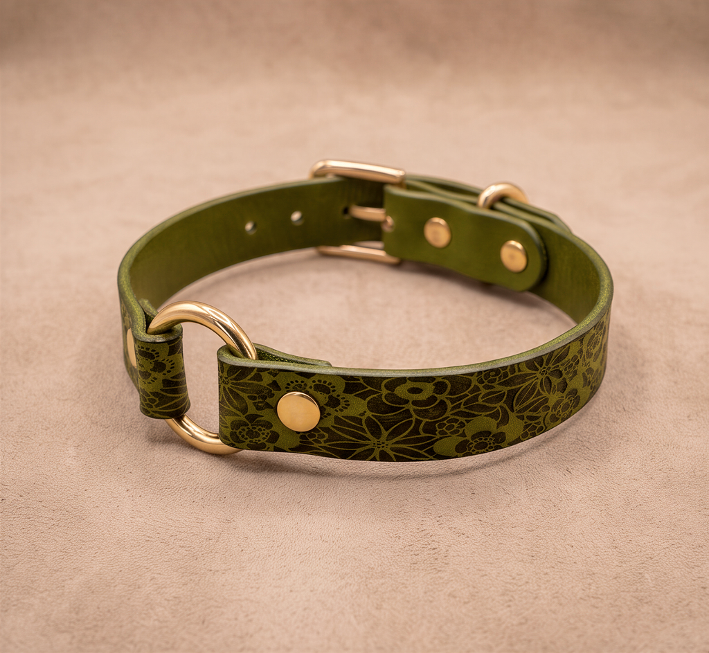 A green leather collar with a floral pattern and gold hardware, including a buckle and two rings, is displayed on a beige background.