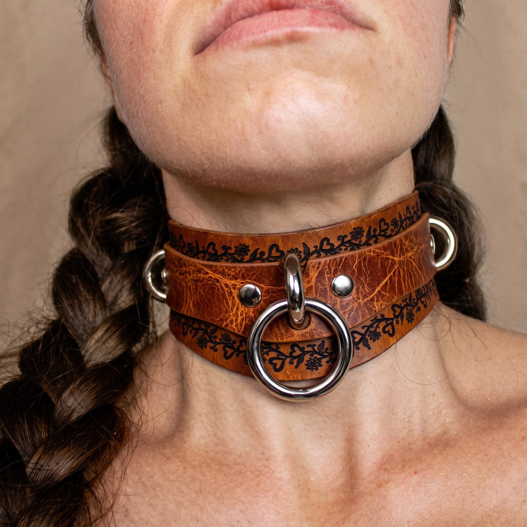 A close-up of a woman's neck and chin wearing a leather choker necklace with metal rings and a metal ring.