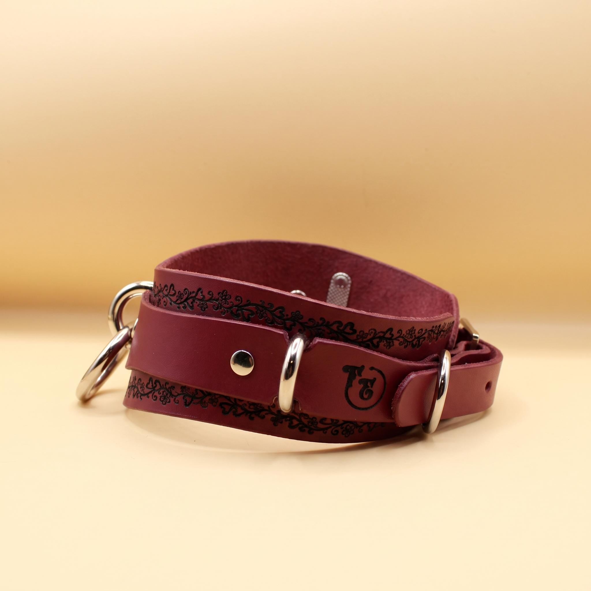 A burgundy leather choker collar with metal rings and a logo on the front.