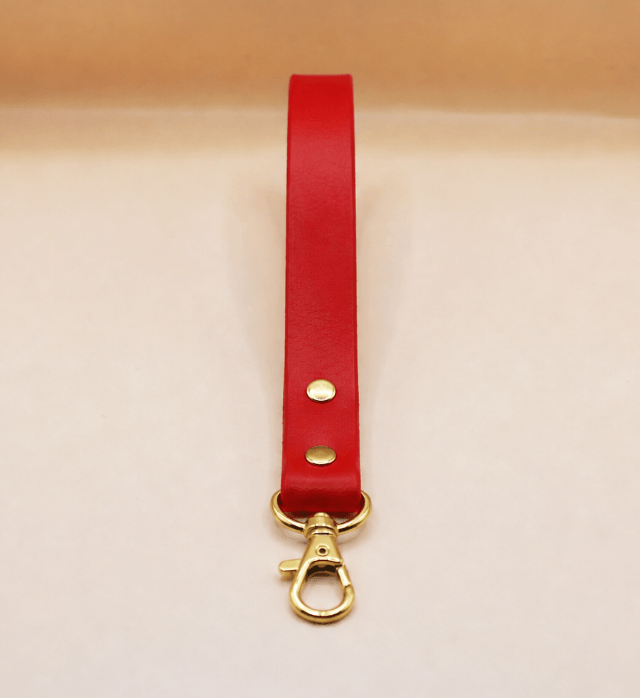 A red leather strap with a gold metal clasp and hook is shown against a light background.