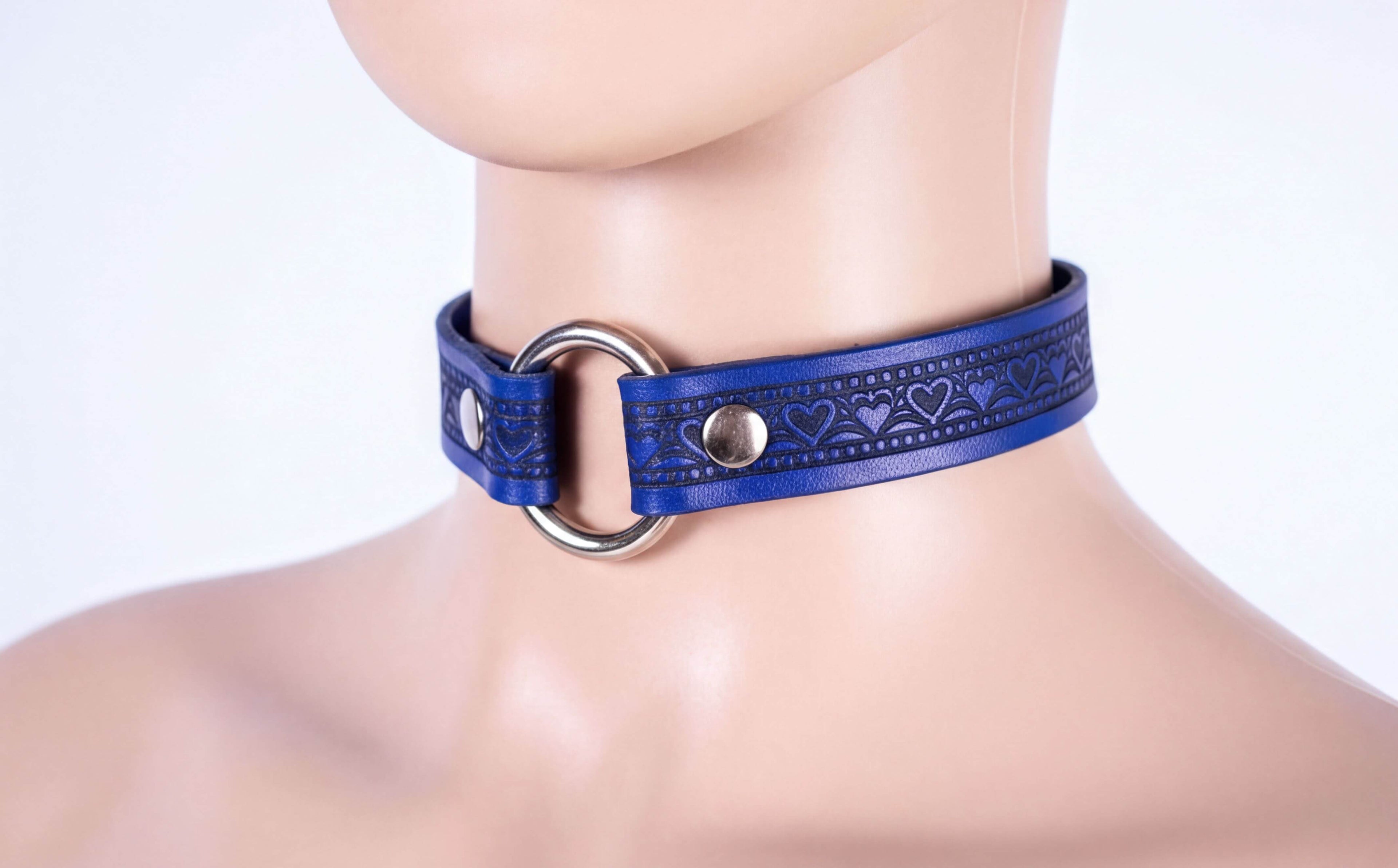 A mannequin head wearing a blue choker necklace with a metal ring and heart-shaped embellishments.