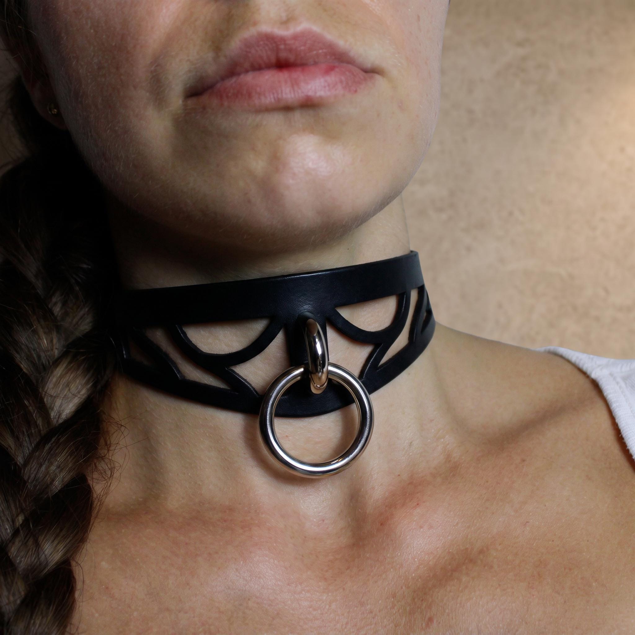 A close-up of a woman's neck and chest area, featuring a black choker necklace with a metal ring and a braided hairstyle.