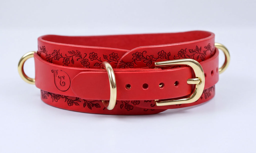 A red leather belt with a floral pattern and a gold buckle.