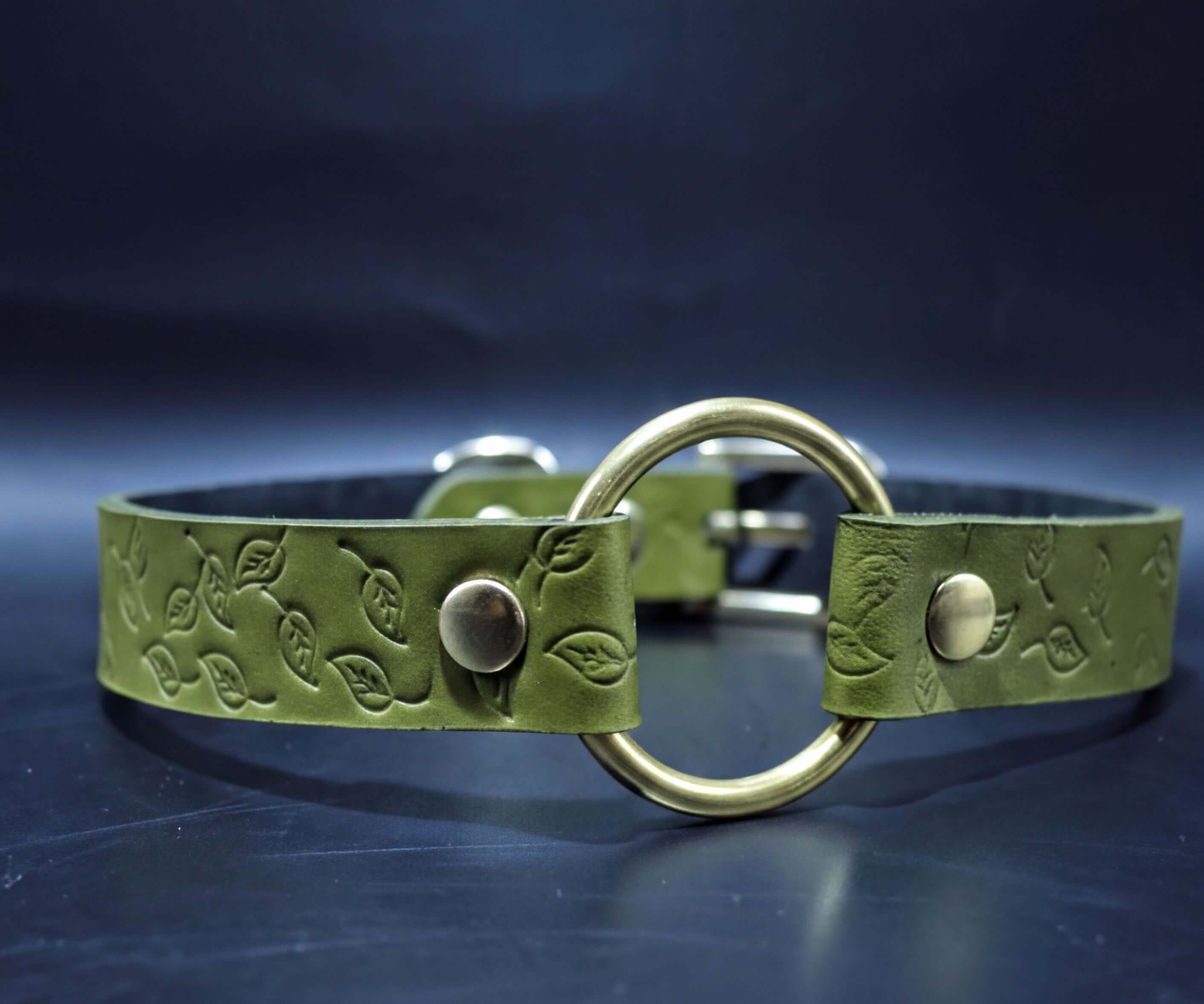 A green leather belt with a round metal buckle and leaf-shaped embossed pattern.