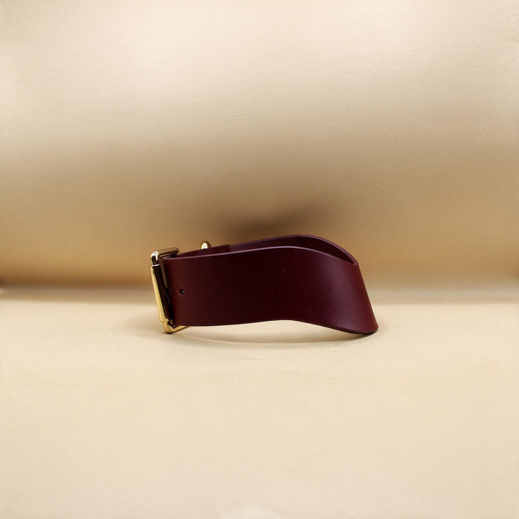 A burgundy leather belt with a gold buckle is shown against a beige background.