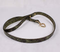 A green leather belt with a heart-shaped charm attached, lying on a white surface.