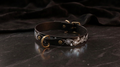 A black leather collar with a floral design and a gold buckle is displayed on a dark surface.
