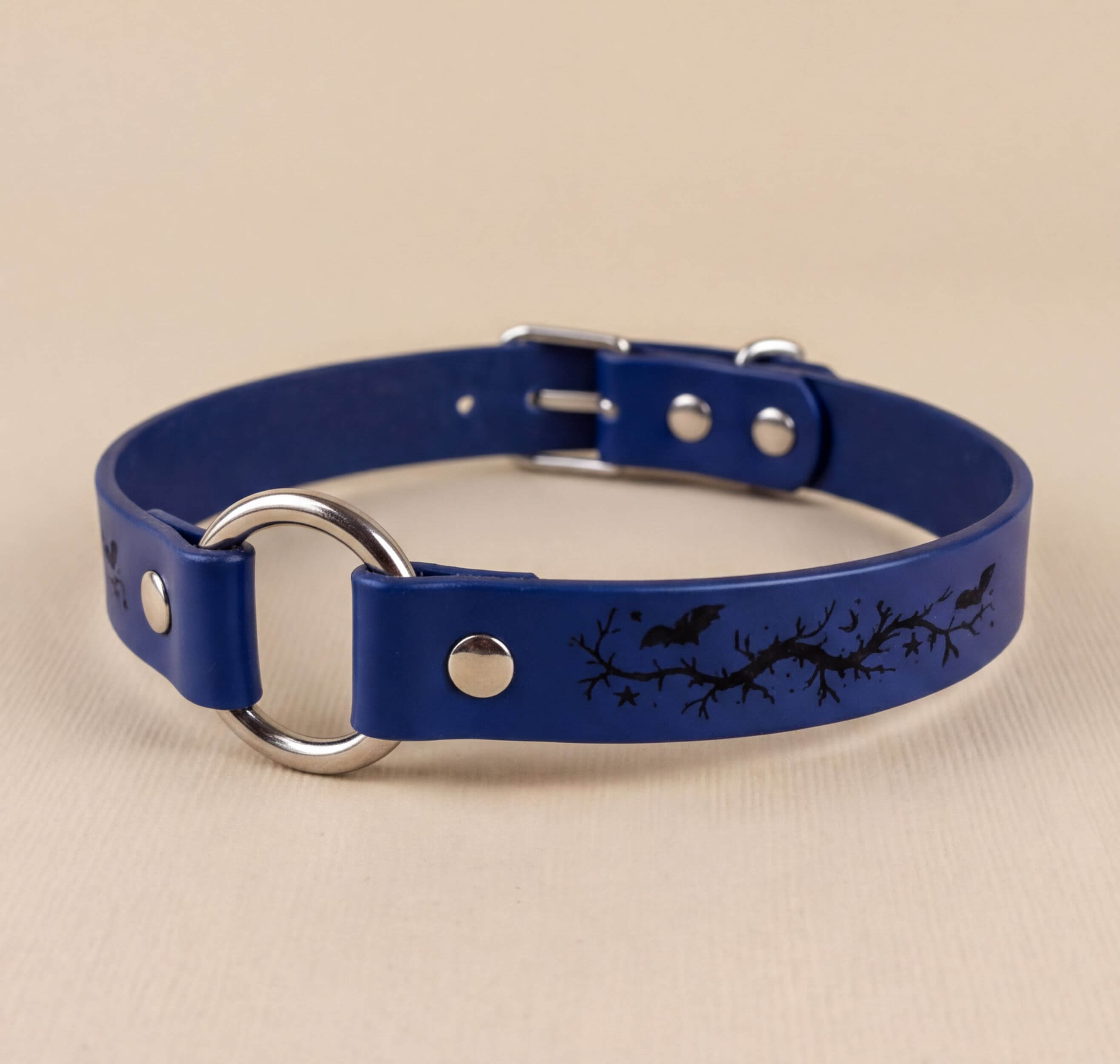 A blue leather collar with a silver ring and a black bat and branch design printed on it.