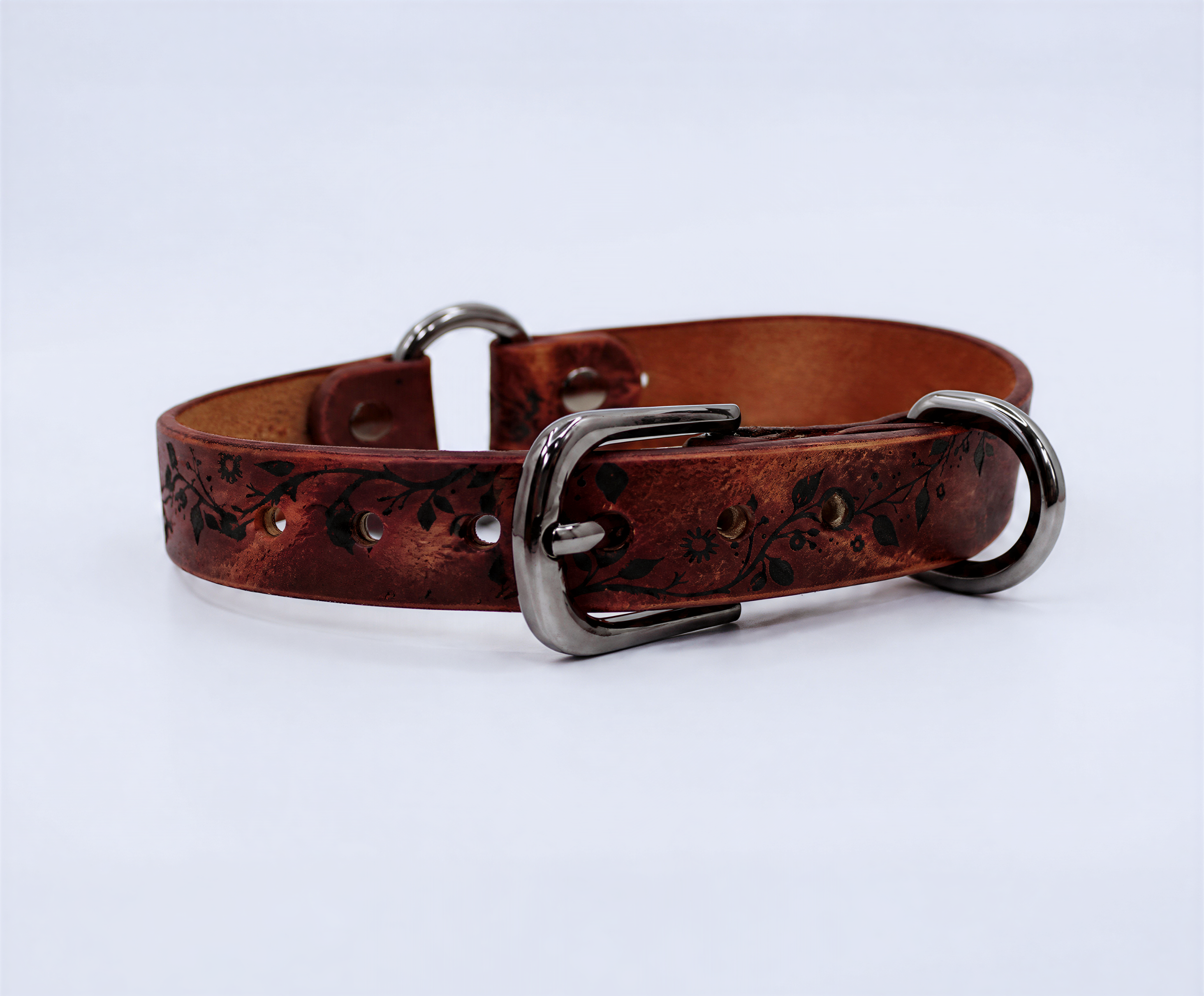 A brown leather dog collar with a metal buckle and decorative pattern on the surface.