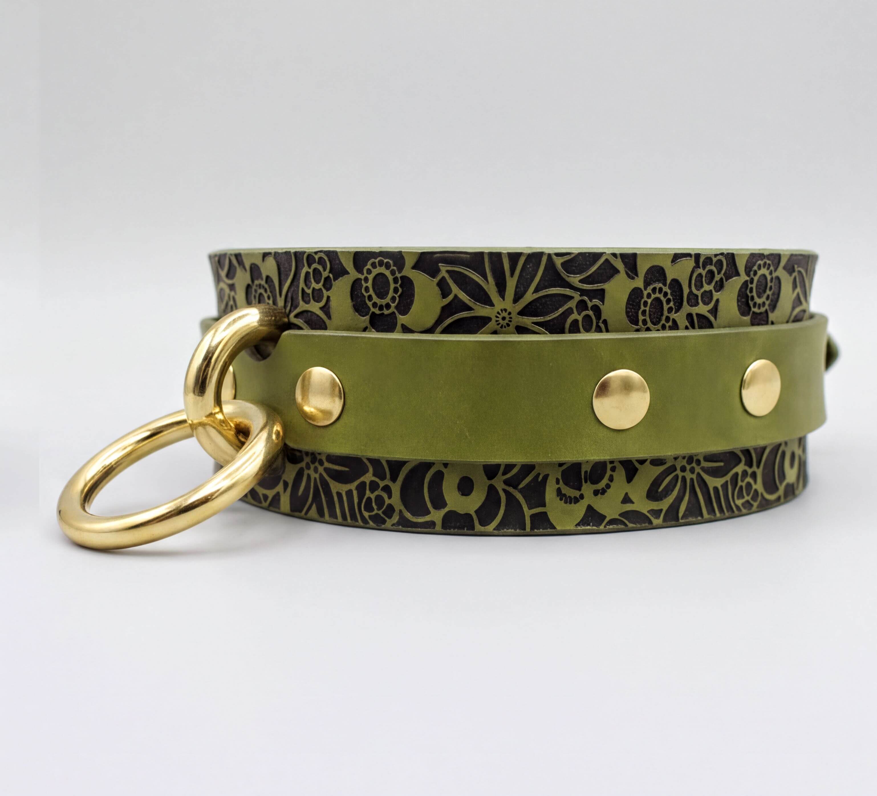 A green leather choker necklace with a floral pattern and gold-colored metal rings.
