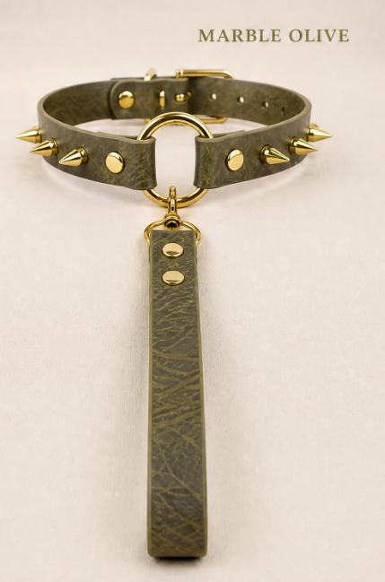 A dark green leather collar with spikes and a gold-colored metal ring, accompanied by a long strap or handle.