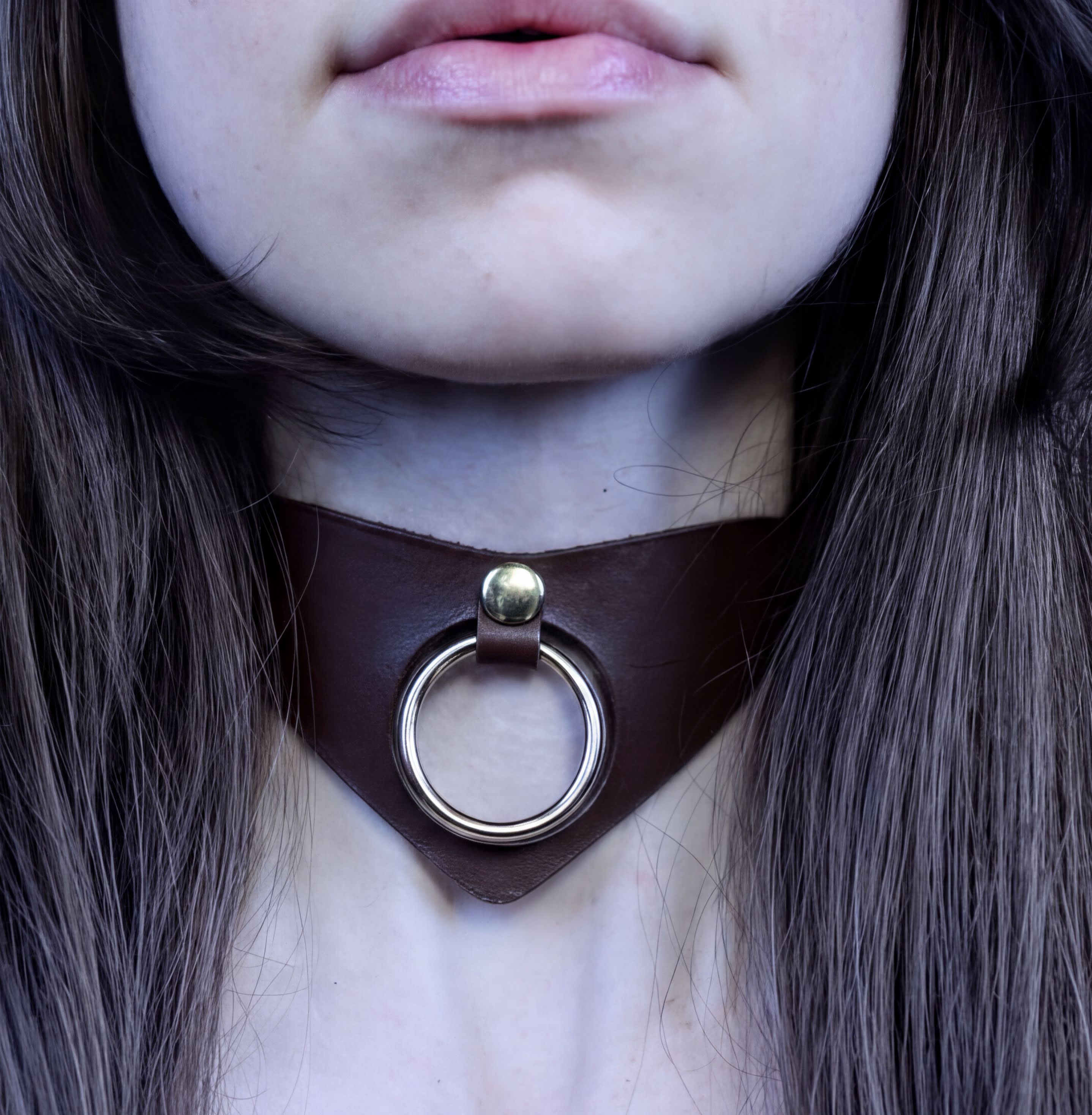 A close-up of a person's neck and chest area, featuring a dark brown leather choker necklace with a metal ring.