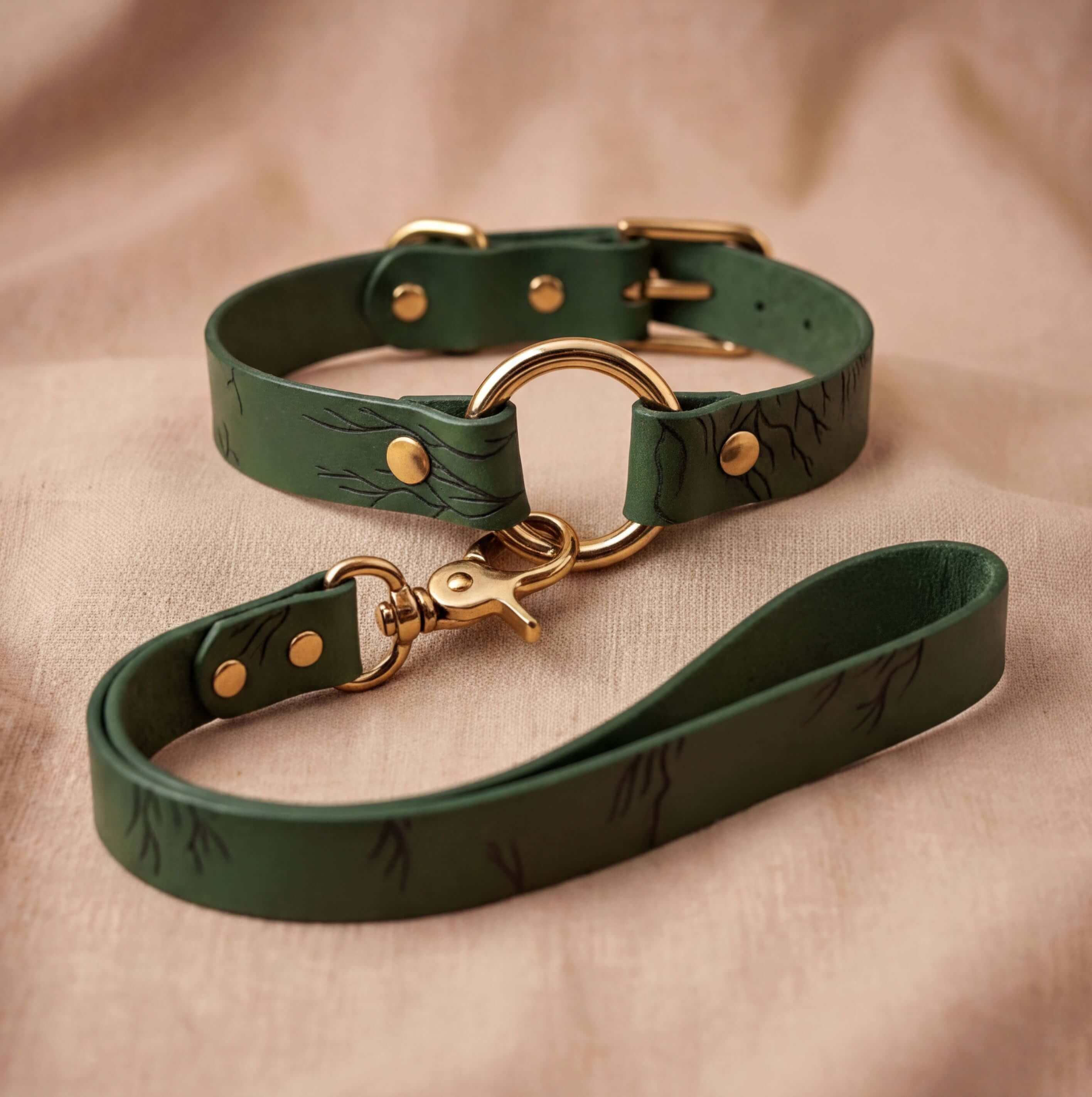 A green leather dog collar with a gold-colored buckle and a matching green leash with a gold-colored buckle are displayed on a beige fabric background.