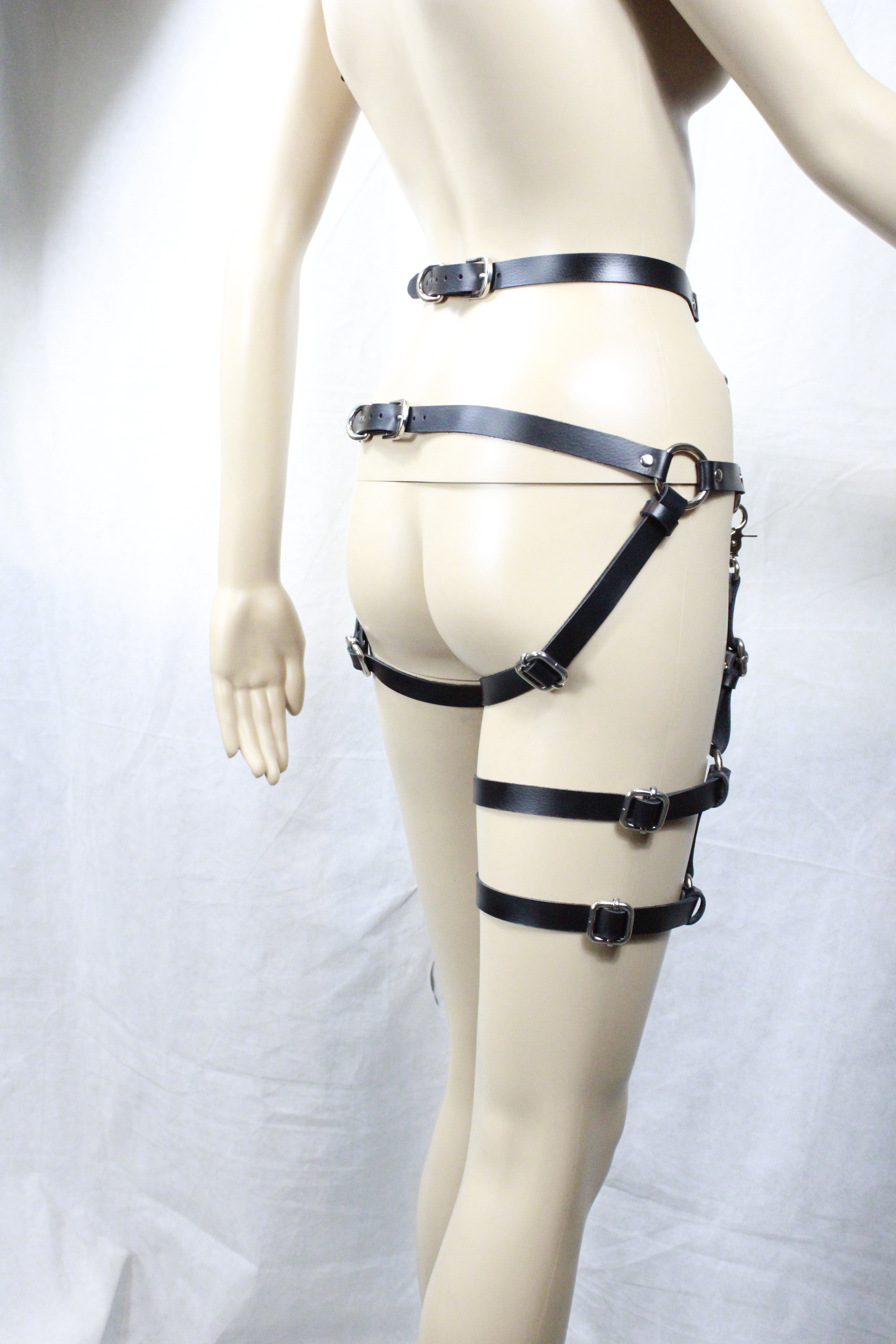 A mannequin wearing a leather strap harness with multiple straps, posing in a relaxed position.