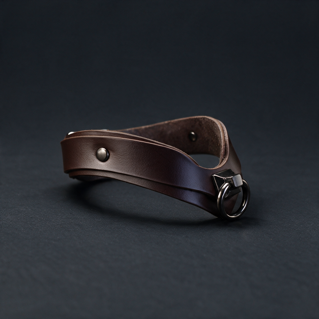 A brown leather choker necklace with a metal clasp and buckle is shown against a dark background.