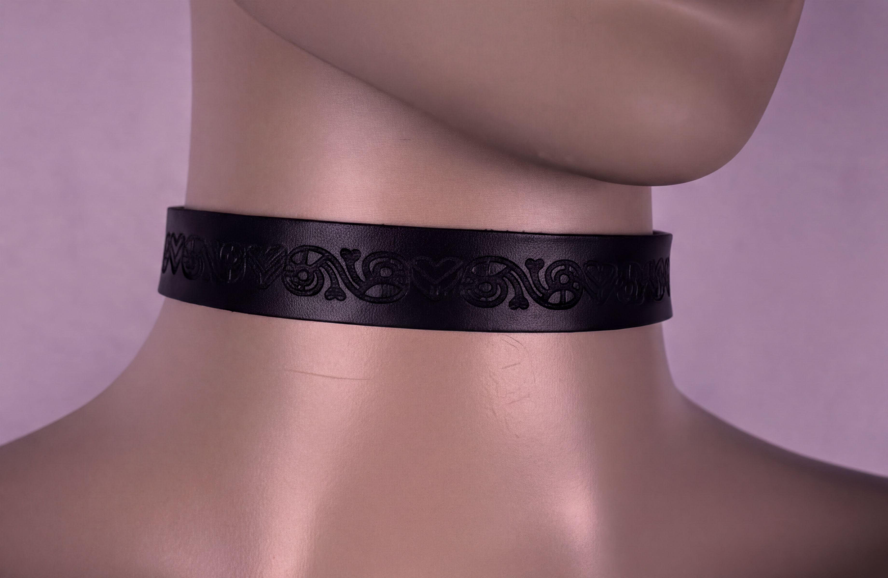 A mannequin head wearing a black choker necklace with a decorative pattern.