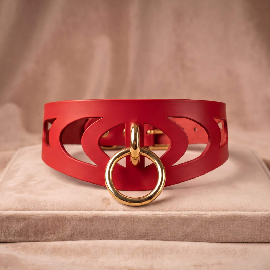 A red leather choker necklace with a gold-colored metal ring and a cutout design on the front.