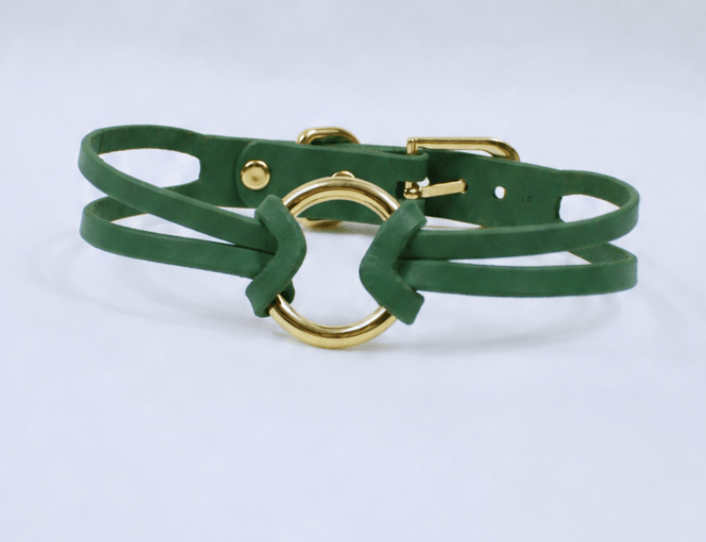 A green leather bracelet with a gold-colored buckle and a circular clasp.